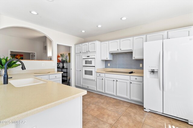 kitchen with white cabinetry, sink, kitchen peninsula, white dishwasher, and light tile patterned floors