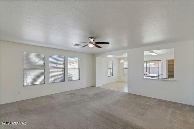 carpeted empty room featuring ceiling fan, sink, a textured ceiling, and a healthy amount of sunlight