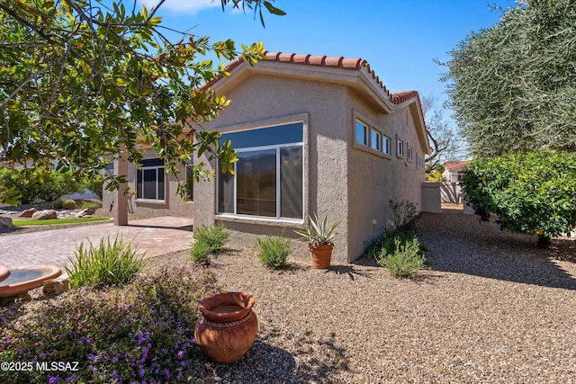 rear view of house with stucco siding, a tile roof, and a patio area