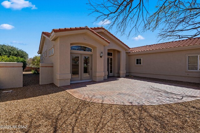 rear view of house featuring a patio area, stucco siding, french doors, and a tile roof