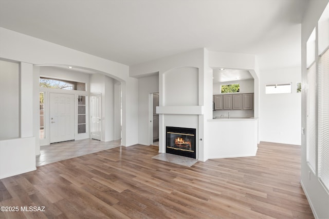 unfurnished living room featuring a fireplace with flush hearth, light wood-style floors, and a healthy amount of sunlight