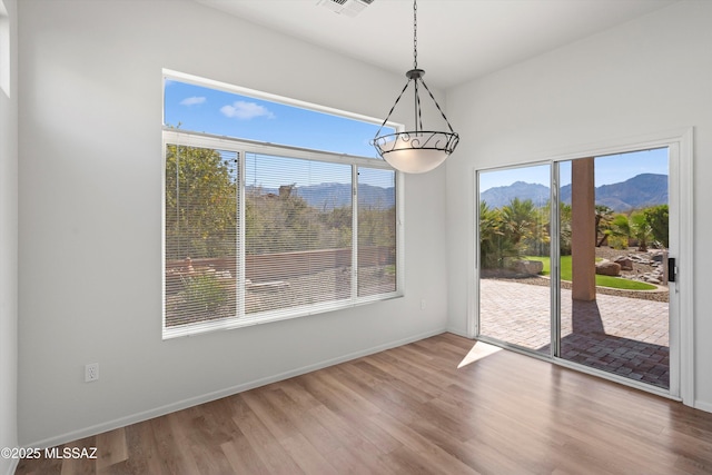 unfurnished dining area featuring visible vents, a notable chandelier, wood finished floors, a mountain view, and baseboards