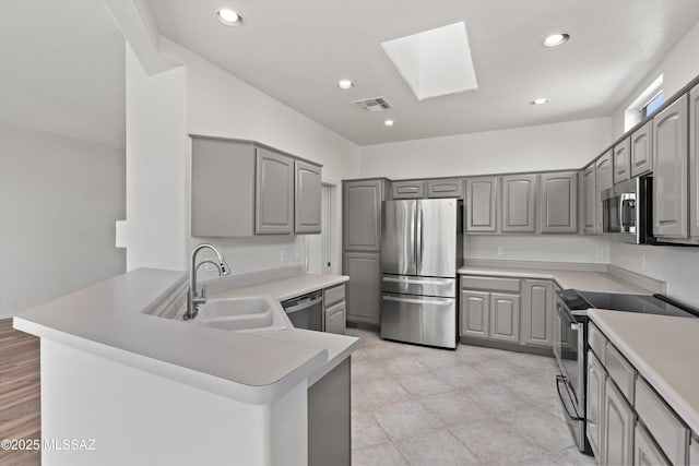 kitchen with visible vents, gray cabinets, a skylight, stainless steel appliances, and a sink