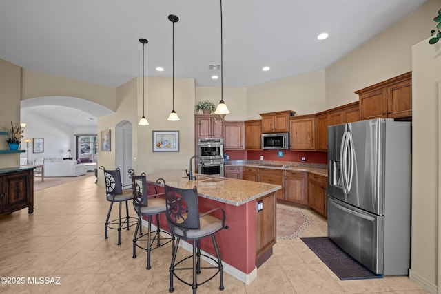 kitchen featuring a kitchen breakfast bar, pendant lighting, light stone countertops, a kitchen island with sink, and stainless steel appliances