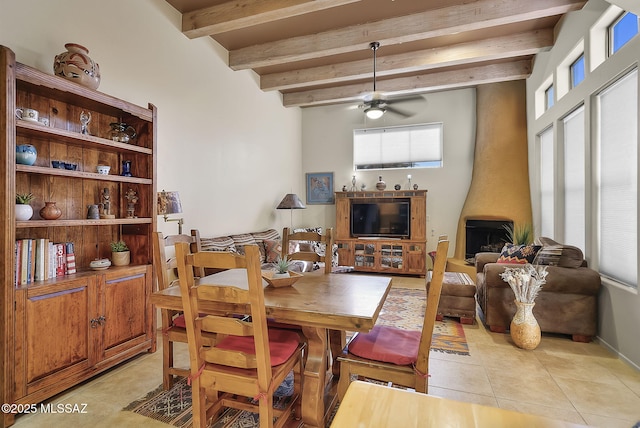 dining room with beamed ceiling, ceiling fan, a wood stove, and light tile patterned floors