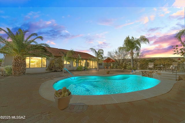 pool at dusk with a patio area