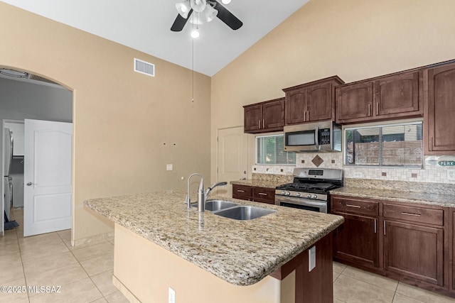 kitchen with light tile patterned floors, sink, appliances with stainless steel finishes, and a kitchen island with sink