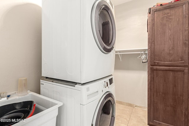 laundry room with light tile patterned floors, sink, stacked washer / drying machine, and cabinets