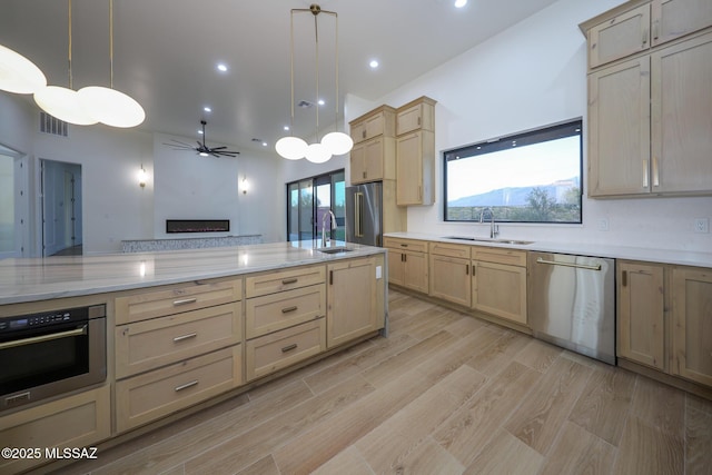 kitchen featuring sink, light brown cabinetry, hanging light fixtures, and stainless steel appliances