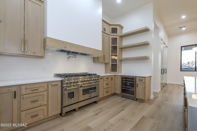 kitchen featuring light brown cabinets, custom range hood, light wood-type flooring, range with two ovens, and beverage cooler