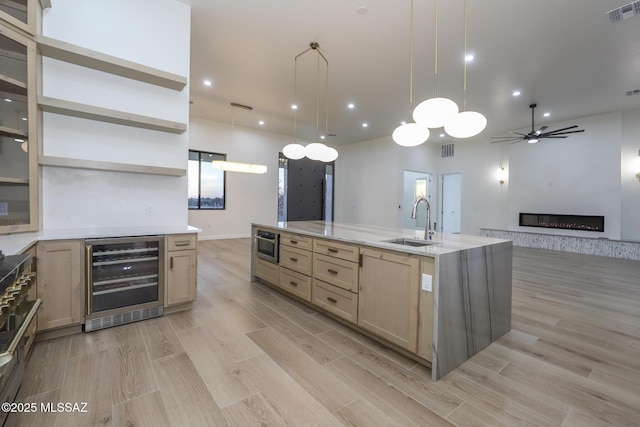 kitchen featuring pendant lighting, light brown cabinetry, sink, a stone fireplace, and beverage cooler