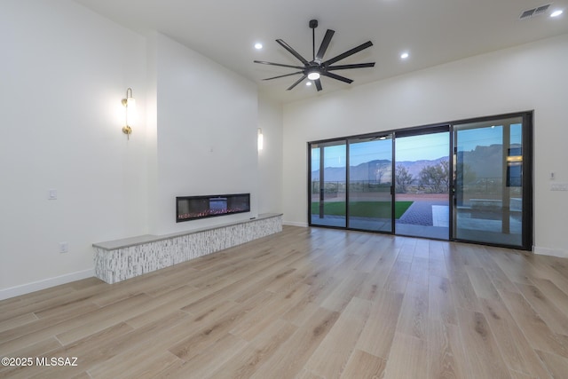 unfurnished living room with a mountain view, ceiling fan, and light wood-type flooring