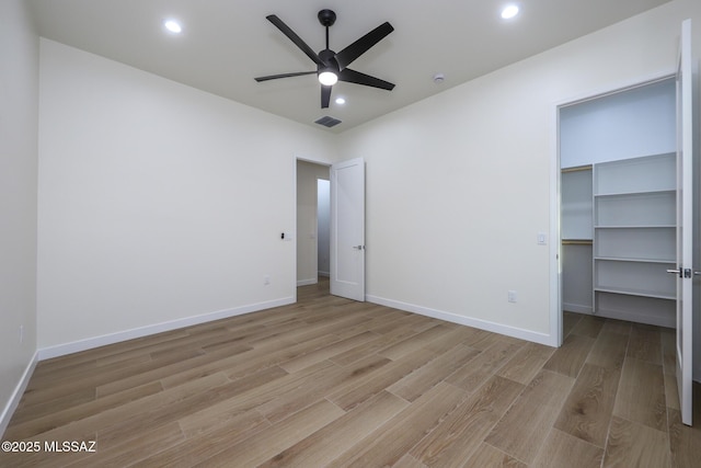 unfurnished bedroom featuring light wood-type flooring, a closet, ceiling fan, and a walk in closet