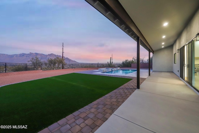 pool at dusk with a patio area, a mountain view, and a lawn