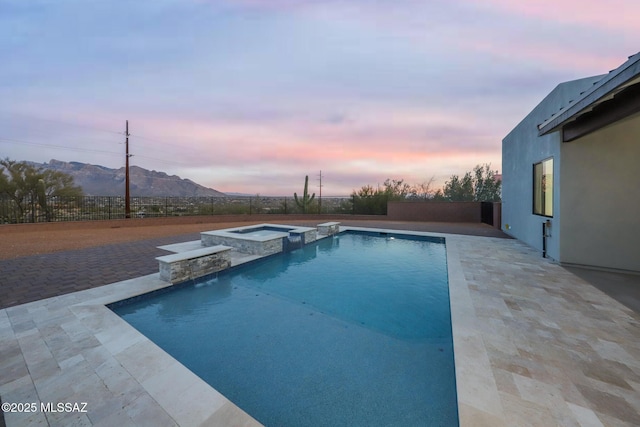 pool at dusk with an in ground hot tub, a patio area, and a mountain view