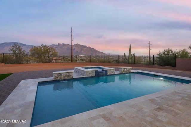 pool at dusk featuring a mountain view, a patio area, an in ground hot tub, and pool water feature