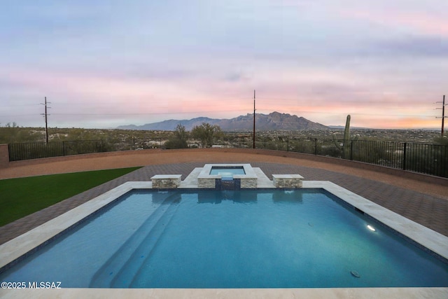 pool at dusk featuring a mountain view and an in ground hot tub