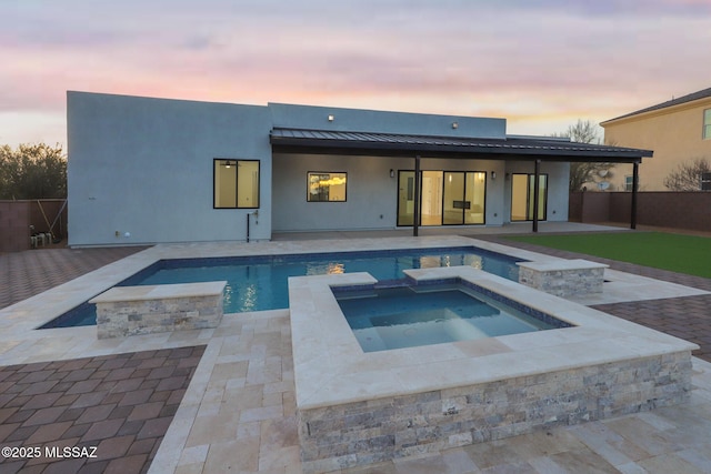 back house at dusk with a pool with hot tub, a patio area, and a fire pit