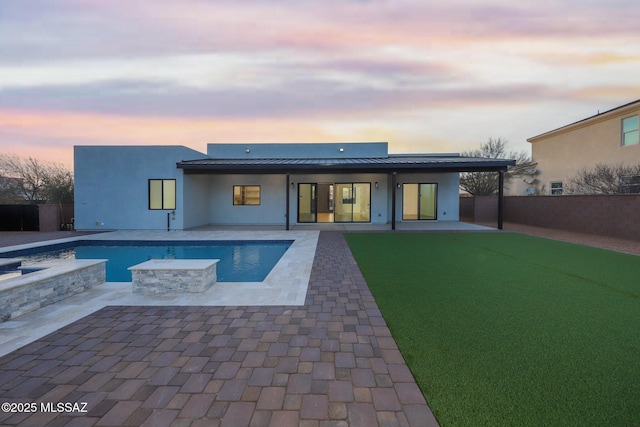 back house at dusk with a swimming pool with hot tub, a patio area, and a lawn