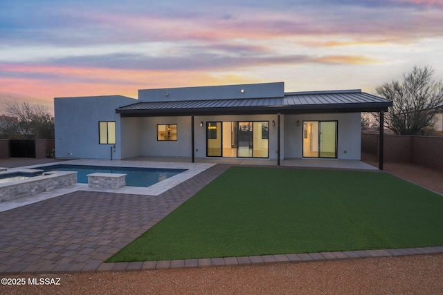 back house at dusk featuring a pool with hot tub, a patio, a yard, and a fire pit