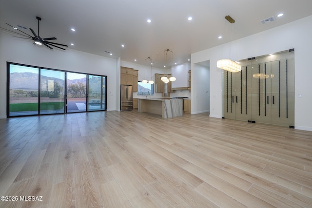 unfurnished living room with a mountain view, ceiling fan, and light wood-type flooring