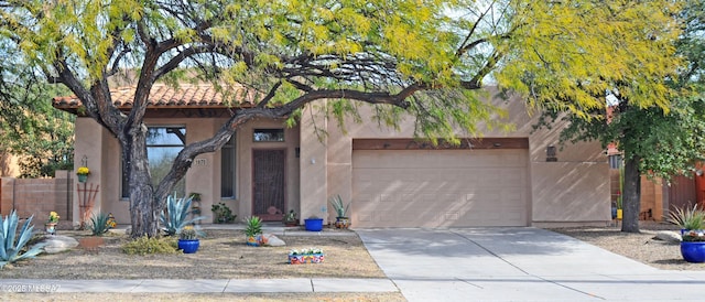 pueblo revival-style home with a tiled roof, stucco siding, driveway, and a garage