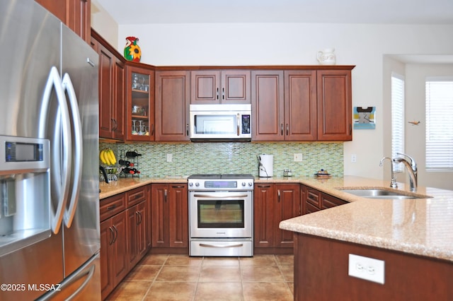 kitchen with a sink, light stone counters, backsplash, appliances with stainless steel finishes, and light tile patterned flooring