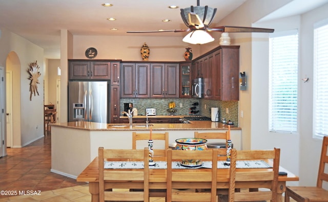 kitchen with a sink, tasteful backsplash, arched walkways, appliances with stainless steel finishes, and glass insert cabinets