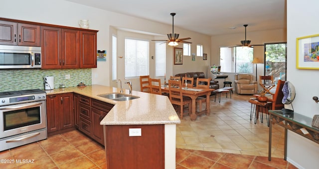 kitchen with light stone countertops, a peninsula, a sink, decorative backsplash, and stainless steel appliances