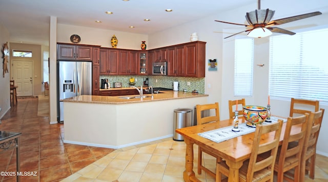 kitchen with a peninsula, light tile patterned flooring, stainless steel appliances, glass insert cabinets, and tasteful backsplash