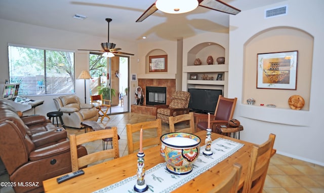 dining space featuring built in features, visible vents, a tiled fireplace, and light tile patterned floors