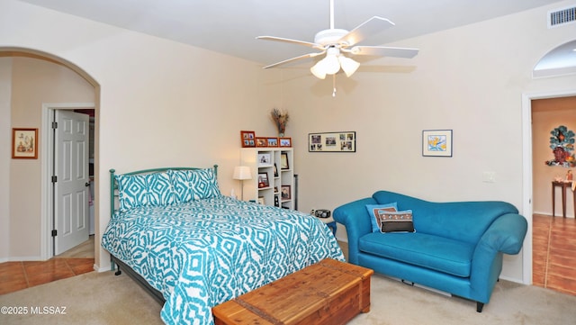 carpeted bedroom featuring arched walkways, visible vents, tile patterned floors, and a ceiling fan