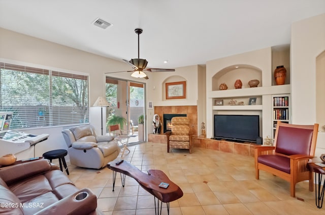 living room with built in features, visible vents, light tile patterned flooring, ceiling fan, and a tile fireplace