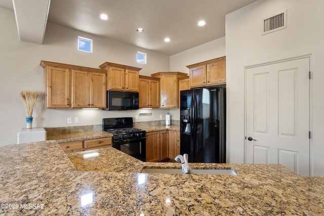 kitchen with light stone counters, sink, black appliances, and kitchen peninsula