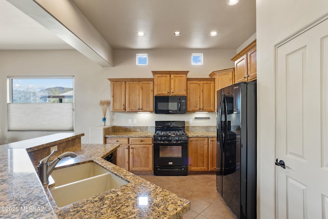 kitchen featuring a sink, light tile patterned flooring, recessed lighting, light stone counters, and black appliances