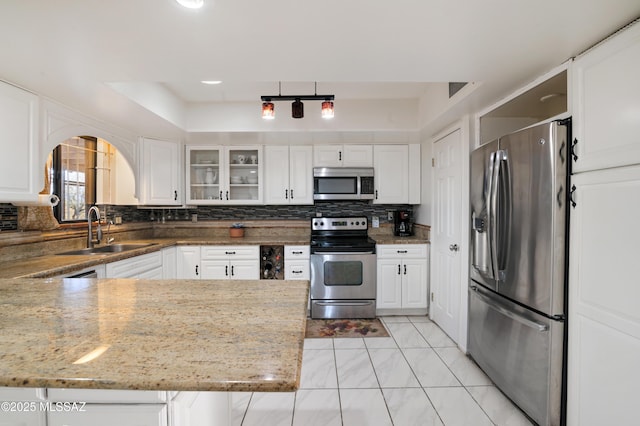 kitchen with sink, appliances with stainless steel finishes, light stone counters, white cabinets, and a raised ceiling