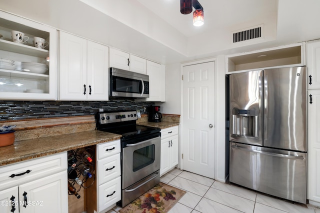 kitchen with appliances with stainless steel finishes, white cabinetry, tasteful backsplash, light tile patterned flooring, and dark stone counters