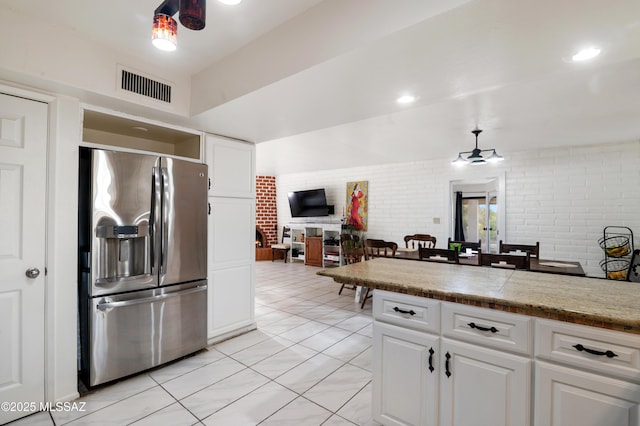 kitchen with white cabinetry, ceiling fan, brick wall, and stainless steel refrigerator with ice dispenser