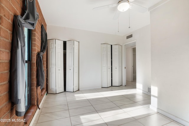 unfurnished bedroom with multiple closets, brick wall, and ceiling fan