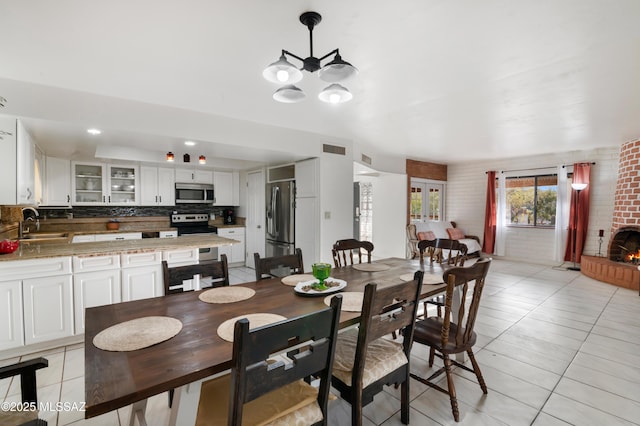 tiled dining space featuring sink, a chandelier, and a brick fireplace