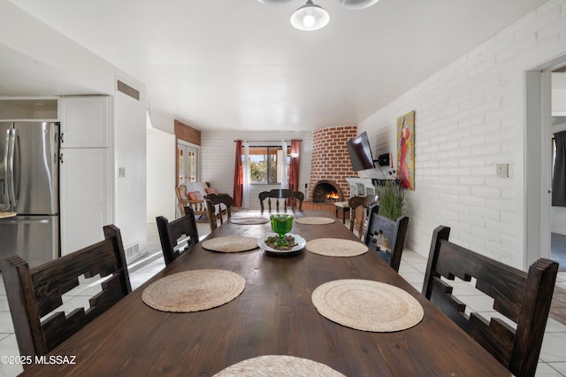 dining room with light tile patterned flooring, brick wall, and a brick fireplace