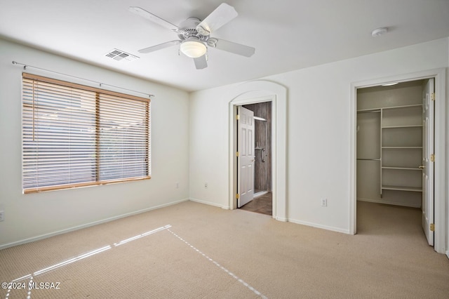 unfurnished bedroom with connected bathroom, a walk in closet, light carpet, a closet, and ceiling fan