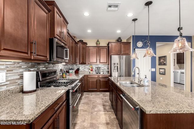 kitchen with sink, hanging light fixtures, stainless steel appliances, washing machine and dryer, and a center island with sink