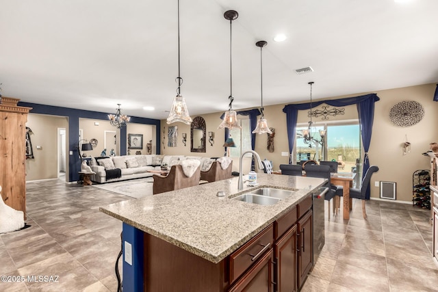 kitchen with decorative light fixtures, sink, a kitchen island with sink, stainless steel dishwasher, and light stone countertops