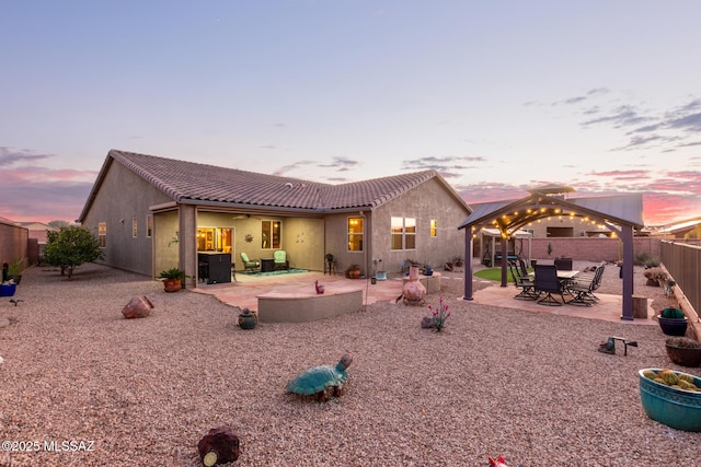 back house at dusk featuring a gazebo and a patio area