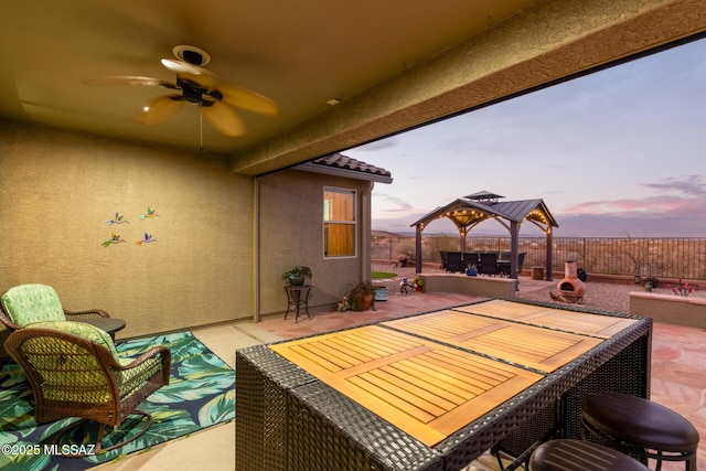 patio terrace at dusk featuring a fire pit, a gazebo, and ceiling fan