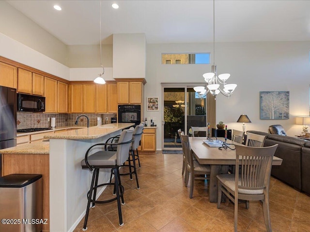 kitchen with light stone counters, hanging light fixtures, decorative backsplash, and black appliances