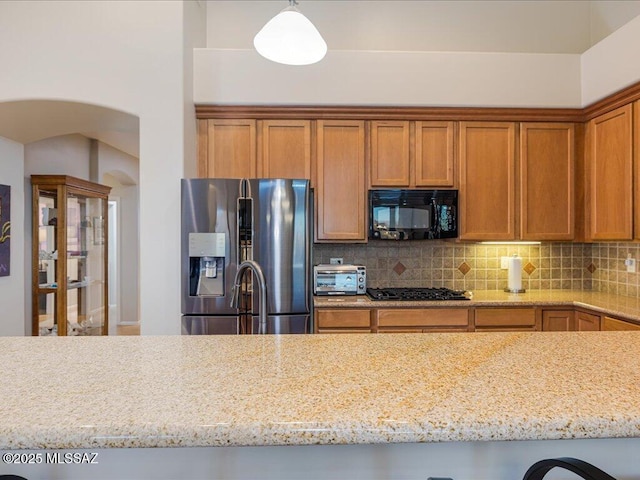 kitchen with light stone countertops, decorative light fixtures, backsplash, and black appliances