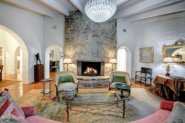 living room with a fireplace, beamed ceiling, a high ceiling, light tile patterned floors, and an inviting chandelier