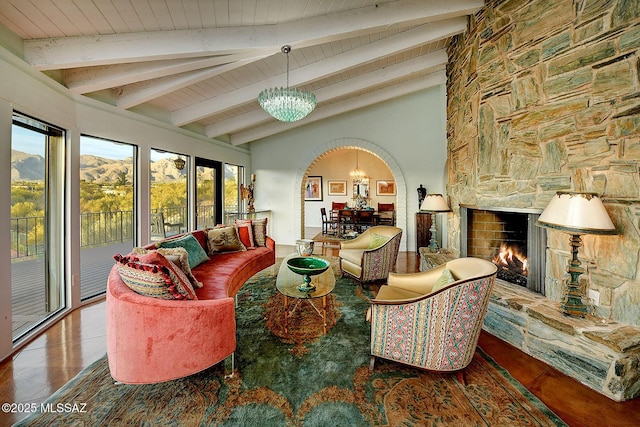 living room featuring beamed ceiling, a stone fireplace, high vaulted ceiling, and an inviting chandelier